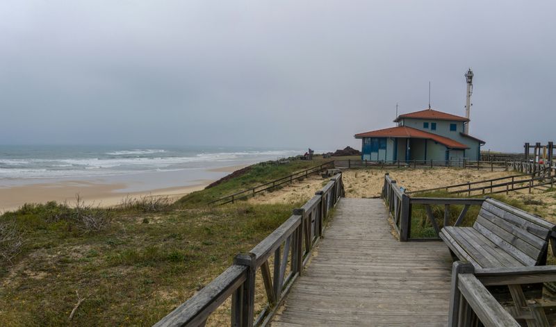 a wooden walkway leading to a beach with a life guard tower in the background